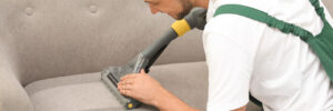 Man performing upholstery cleaning on a warn, stained couch.