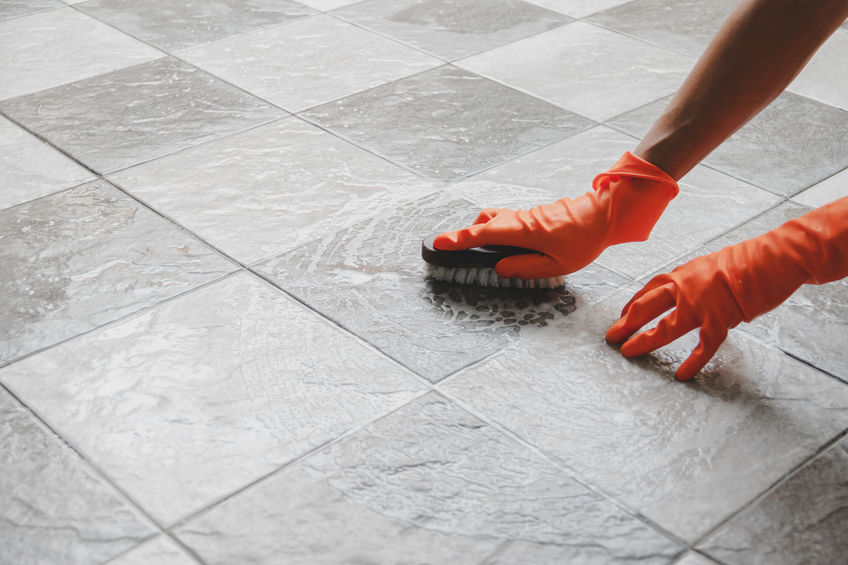 Hand of man wearing orange rubber gloves is used to convert scrub cleaning on the tile floor